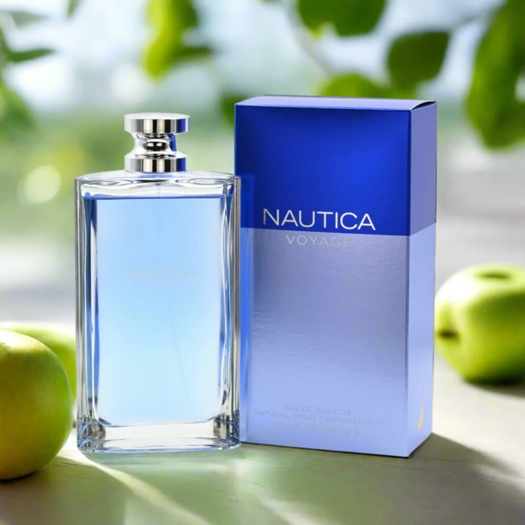 Parfumfles Nautica Voyage met lichtblauwe inhoud naast blauwe verpakking, omringd door groene appels en zachte natuurbokeh.